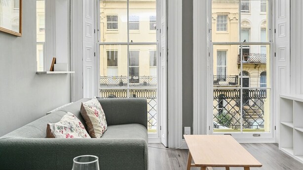 A modern living room with a grey sofa, a wooden coffee table, and large windows offering a view of a cityscape. - Host Stay Sea View Oriental Place (Brighton)
