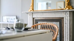 A wicker chair in a room with a fireplace, a mirror, and a table with a bowl and a laptop. - Host Stay Sea View Oriental Place (Brighton)