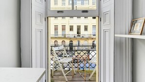 A view from a room with a balcony, featuring a white table, a chair, and a framed picture on a shelf. - Host Stay Sea View Oriental Place (Brighton)