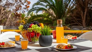 A breakfast table with fruit, juice, and pastries, set outdoors with a view of trees and a railing. - Charming apartment at Vilamoura Marina (Quarteira)