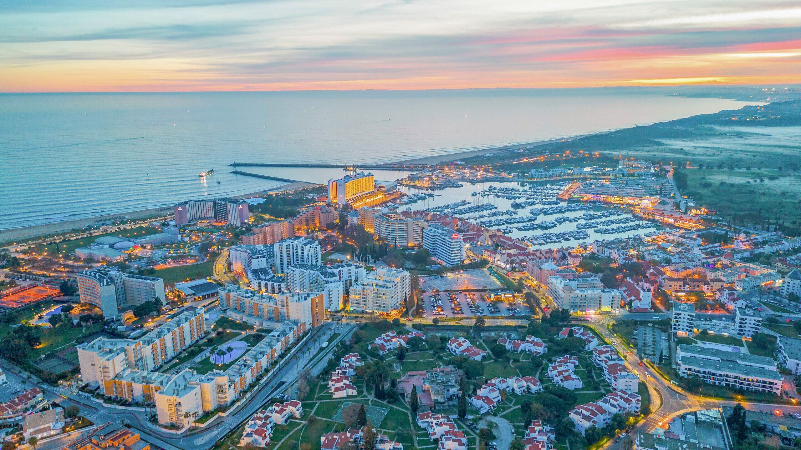An aerial view of a coastal city with a marina, residential areas, and commercial buildings.