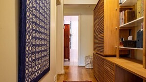 Un couloir orné d’une tapisserie à motifs, avec un tapis rouge et bleu, des étagères en bois et une porte donnant sur une autre pièce.