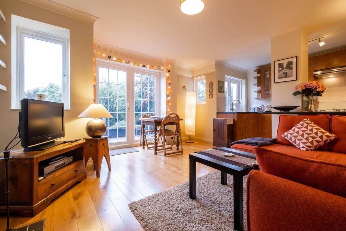 Ein Wohnzimmer mit Fernseher, Sofa und Couchtisch. Es gibt einen Essbereich mit Tisch und Stühlen. Die Küche ist sichtbar, mit Schränken und einem Herd.