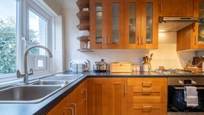 Une cuisine moderne avec des meubles en bois, un évier en acier inoxydable, un four Bosch et une fenêtre laissant entrer la lumière naturelle.