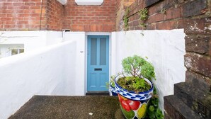 Une ruelle étroite avec une porte bleue, des murs blancs et un pot de fleurs orné d’un motif coloré.