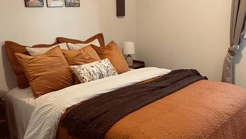 A bedroom with a bed, pillows, a nightstand, a lamp, and wall art.