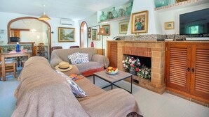 A cozy living room with a sofa, armchairs, a coffee table with a bowl of fruit, a fireplace, and a television. - Can Piña - Two Bedroom Villa, Sleeps 4 (Mallorca)