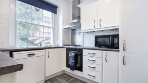 A modern kitchen with white cabinets, a dishwasher, a stove, and a microwave. - |Elegant Three Bed Apt in The Heart of Marylebone| (London)