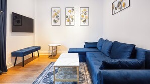 A modern living room with a blue sofa, a white coffee table, a bench, and three framed artworks on the wall. - |Elegant Three Bed Apt in The Heart of Marylebone| (London)