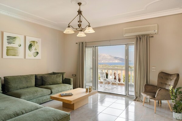 A modern living room with a green sofa, a wooden coffee table, and a view of a balcony with outdoor furniture.