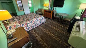 A hotel room with a bed, a desk with a lamp, a chair, a small table, a TV, and a heater. - #33 Nice stay near Bexley and Capital University (Columbus)