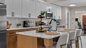 Una cocina con armarios blancos, una isla central con taburetes de bar, un microondas y un refrigerador.