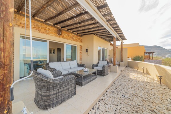 A covered outdoor seating area with wicker furniture, a stone wall, and a view of the landscape. - Oceanview Homes with Terrace (La Paz)