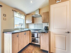 A compact kitchen with wooden cabinets, a gas stove, an oven, and a window with blinds.