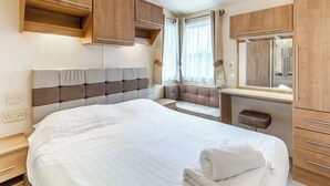 A bedroom with a large bed, wooden headboard, built-in wardrobe, and a window with curtains. - 2 bedroom accommodation in Ilfracombe (Ilfracombe)