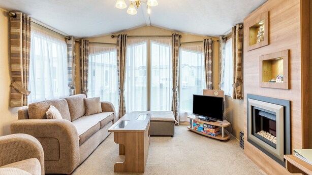 A modern living room with a sofa, coffee table, TV, fireplace, and large windows with curtains. - 2 bedroom accommodation in Ilfracombe (Ilfracombe)