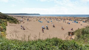 A beach with tents and people, a lifeguard tower, and a distant shoreline. - 2 bedroom accommodation in Ilfracombe (Ilfracombe)