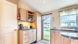 A modern kitchen with wooden cabinets, a microwave, a coffee maker, and a view of a residential area. - 2 bedroom accommodation in Ilfracombe (Ilfracombe)