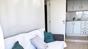 A modern living room with a sofa, two pillows, and a view into a kitchen with cabinets and a countertop. - T1 Torre Azul 10 A C Vista Mar e Praia (Loulé)