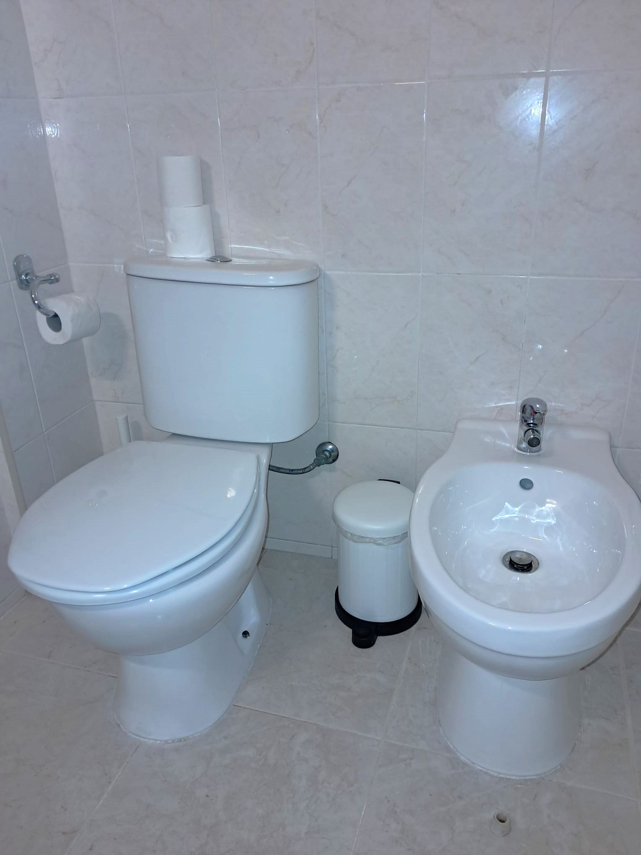 Een badkamer met een toilet, een bidet en een toiletrolhouder.