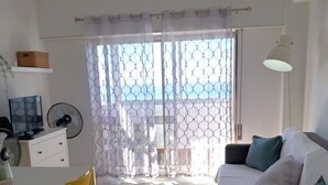 A modern living room with a dining area, a sofa with cushions, a TV, and a fan. - T1 Torre Azul 10 A C Vista Mar e Praia (Loulé)