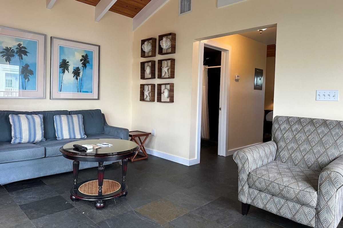 A living room with a sofa, a patterned armchair, a round table, and artwork on the walls.