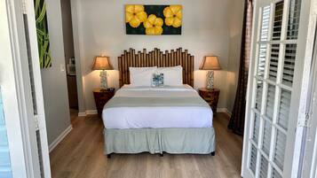 Quarto de hotel com cama, duas mesas de cabeceira com abajures, um ventilador de teto, uma parede com pintura floral e uma porta de vidro deslizante.