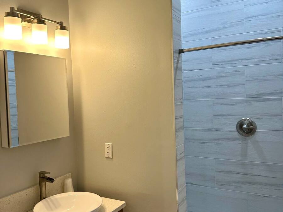 Een badkamer met een wastafel, spiegel en douche met glazen deur.