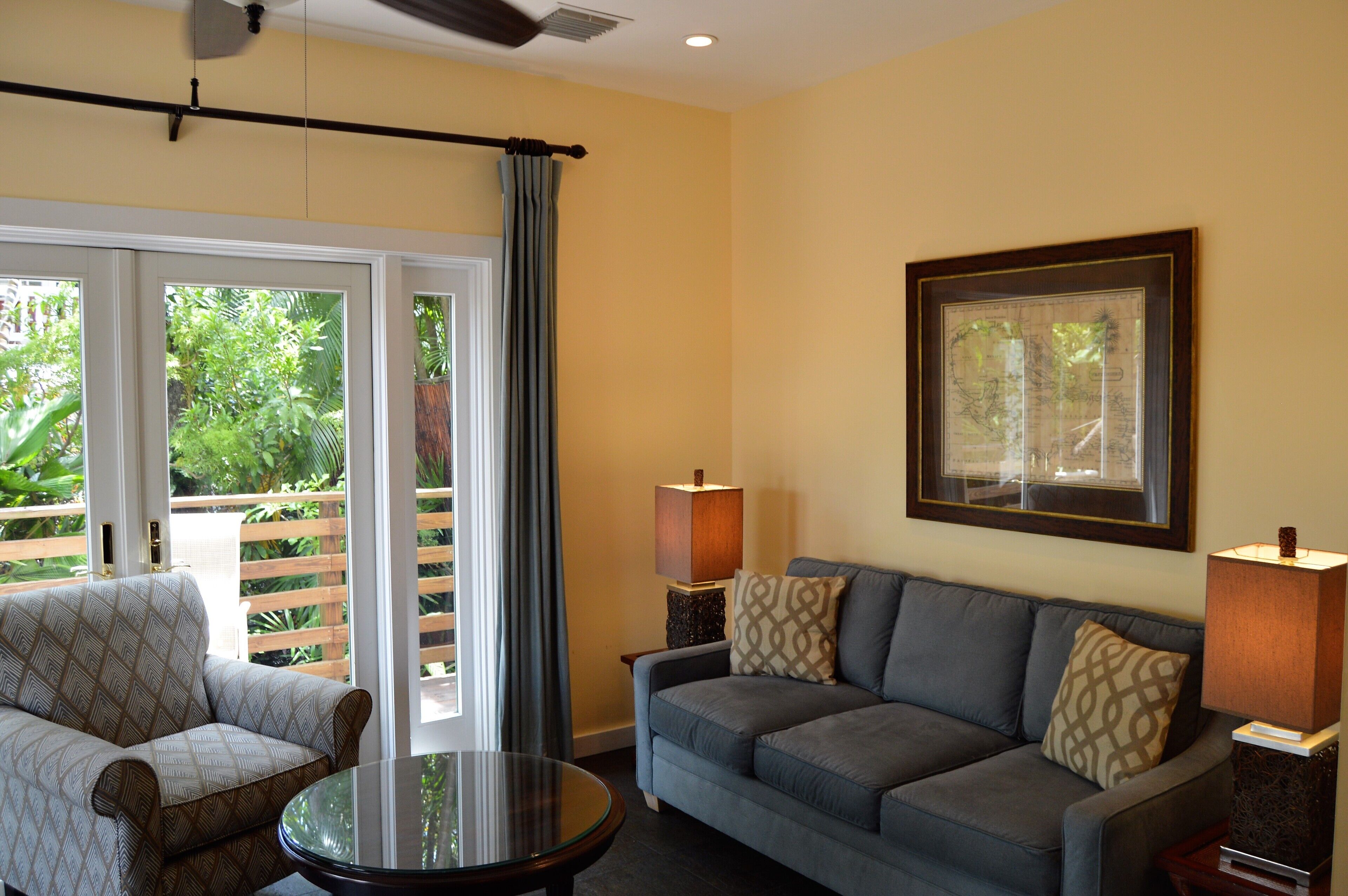 A living room with a sofa, armchair, and a small table. There are two floor lamps and a framed picture on the wall.
