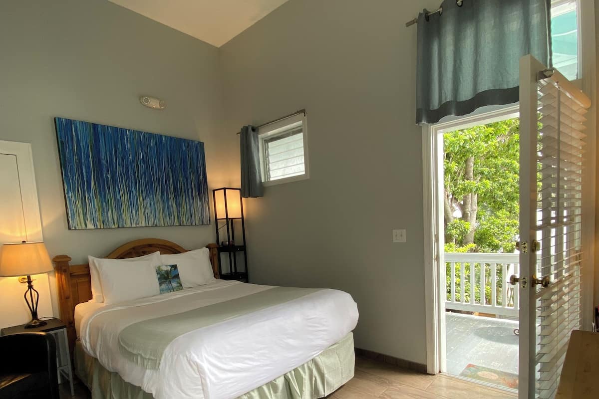 A bedroom with a bed, a ceiling fan, a window with curtains, a nightstand, and a wall-mounted TV.