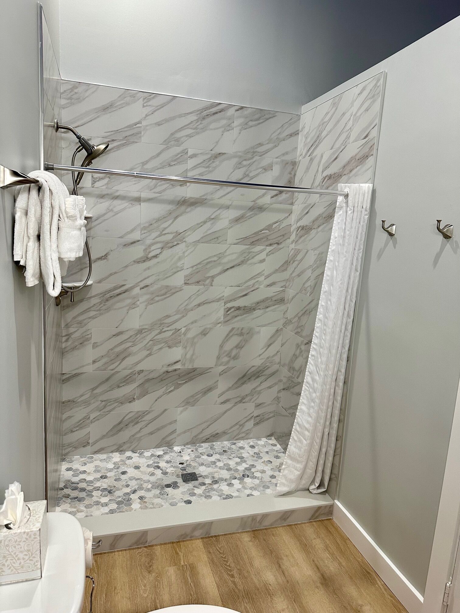 A modern bathroom with a shower area featuring marble tiles, a glass door, and a wooden floor.