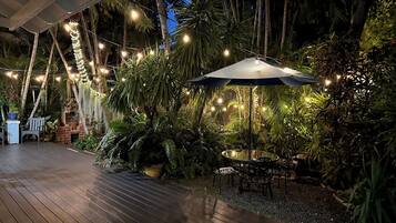 Une terrasse extérieure avec un plancher en bois, une table entourée de chaises, des guirlandes lumineuses et un grand parasol.