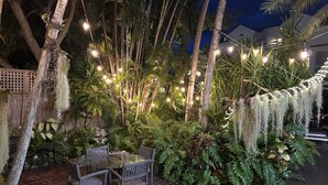 An outdoor patio with a table and chairs, surrounded by lush greenery and string lights. - Douglas House - Adults Only (Key West)