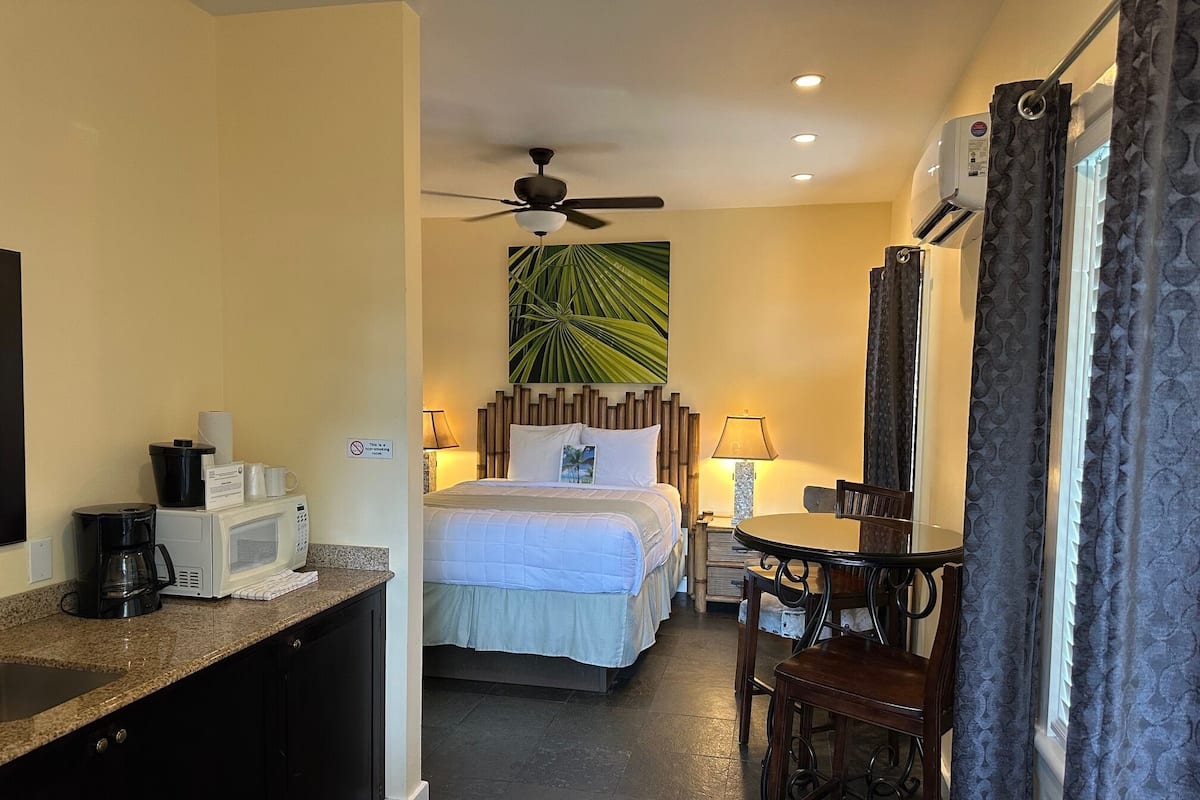 A hotel room with a bed, a desk, a chair, a coffee maker, a microwave, and a ceiling fan.