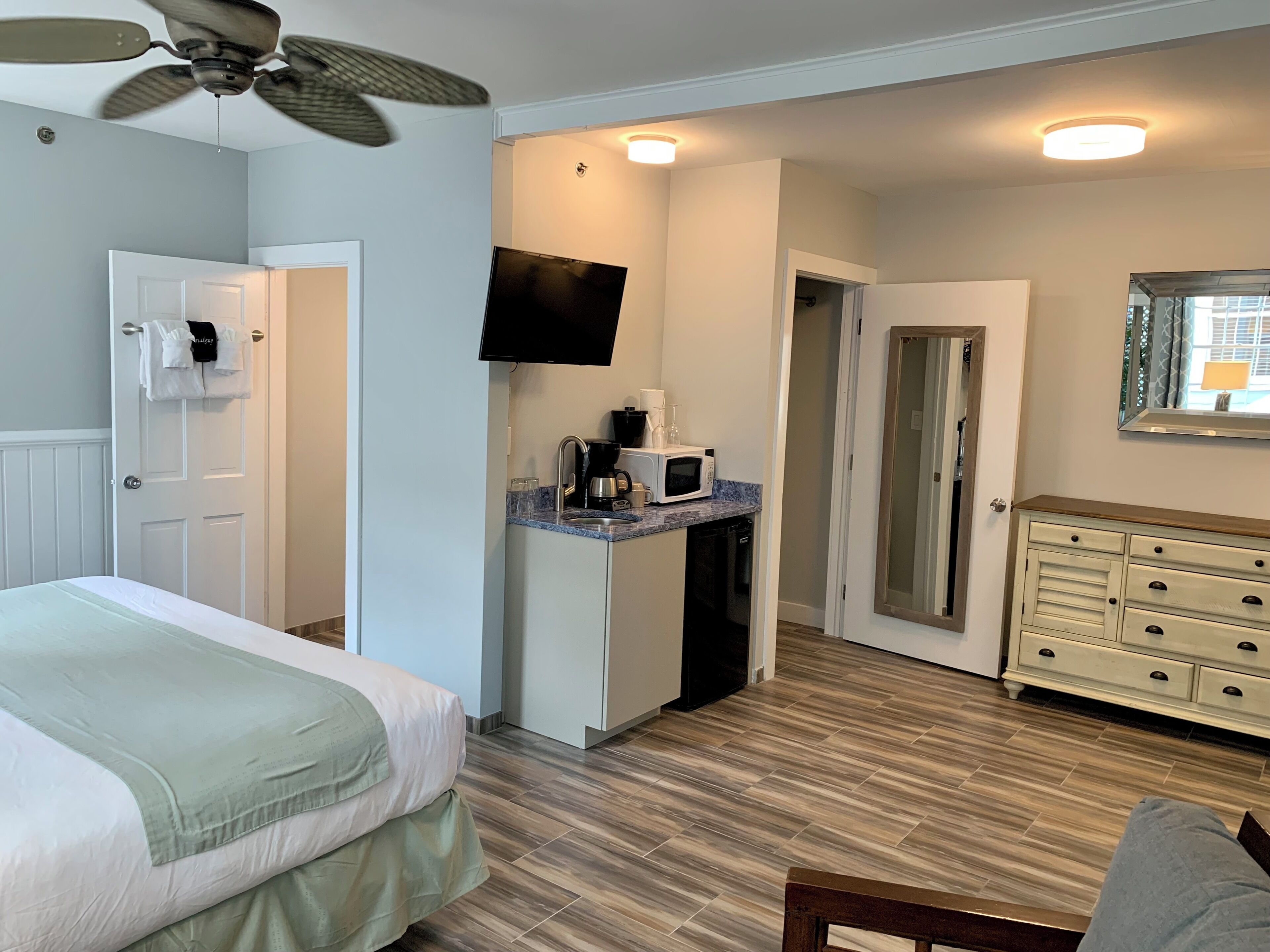 Una habitación de hotel con cama, kitchenette equipada con microondas, ventilador de techo y cómoda.