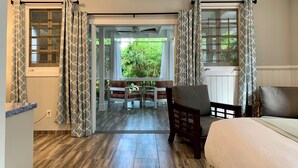 A hotel room with a bed, a wooden floor, a seating area with a table and chairs, and a view of greenery outside. - Douglas House - Adults Only (Key West)