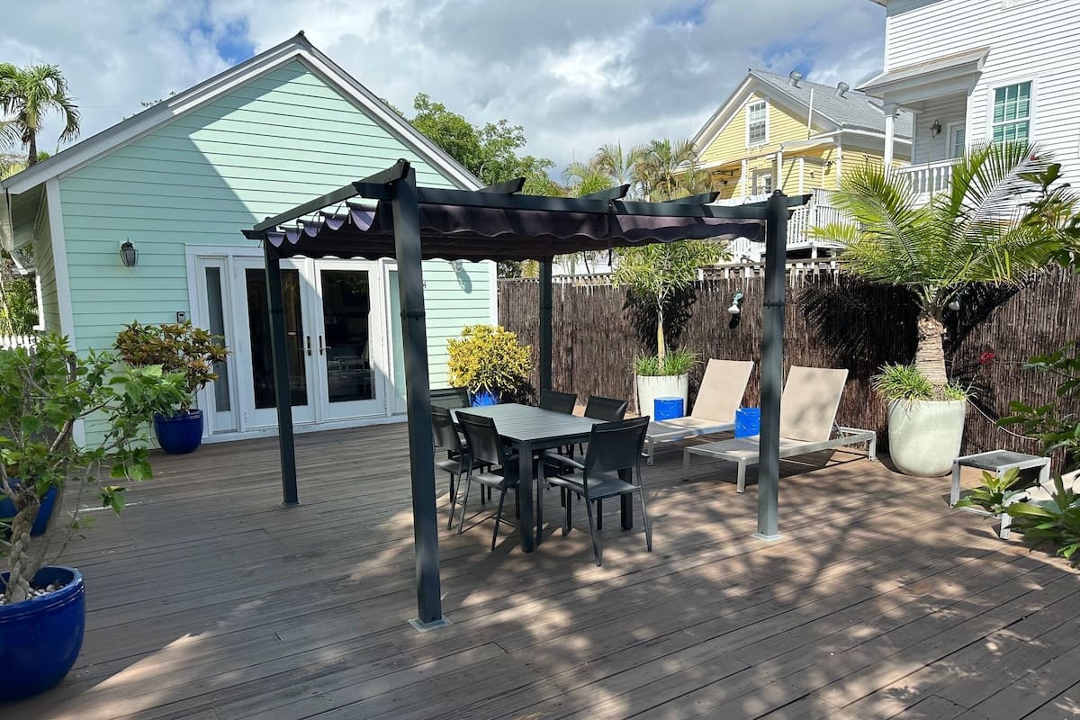 A wooden deck with a pergola, outdoor seating, and potted plants.