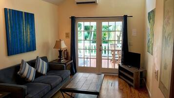 A living room with a sofa, a coffee table, a television, and a sliding glass door leading to an outdoor area.