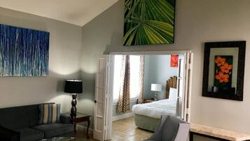A hotel room with a sofa, a chair, a coffee table, a bed, and a painting on the wall.