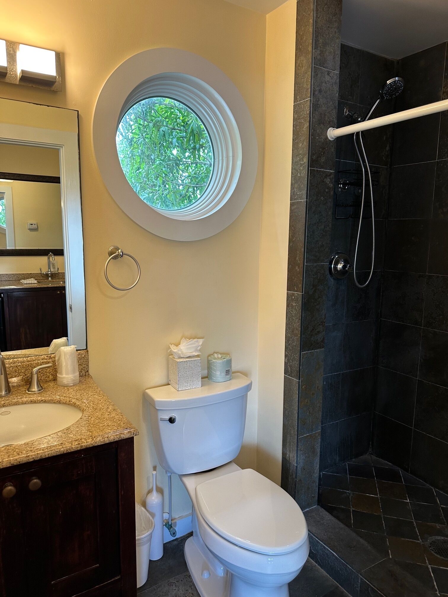 A bathroom with a toilet, sink, and shower. There is a window above the toilet.