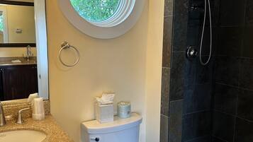 A bathroom with a toilet, sink, and shower. There is a window above the toilet.