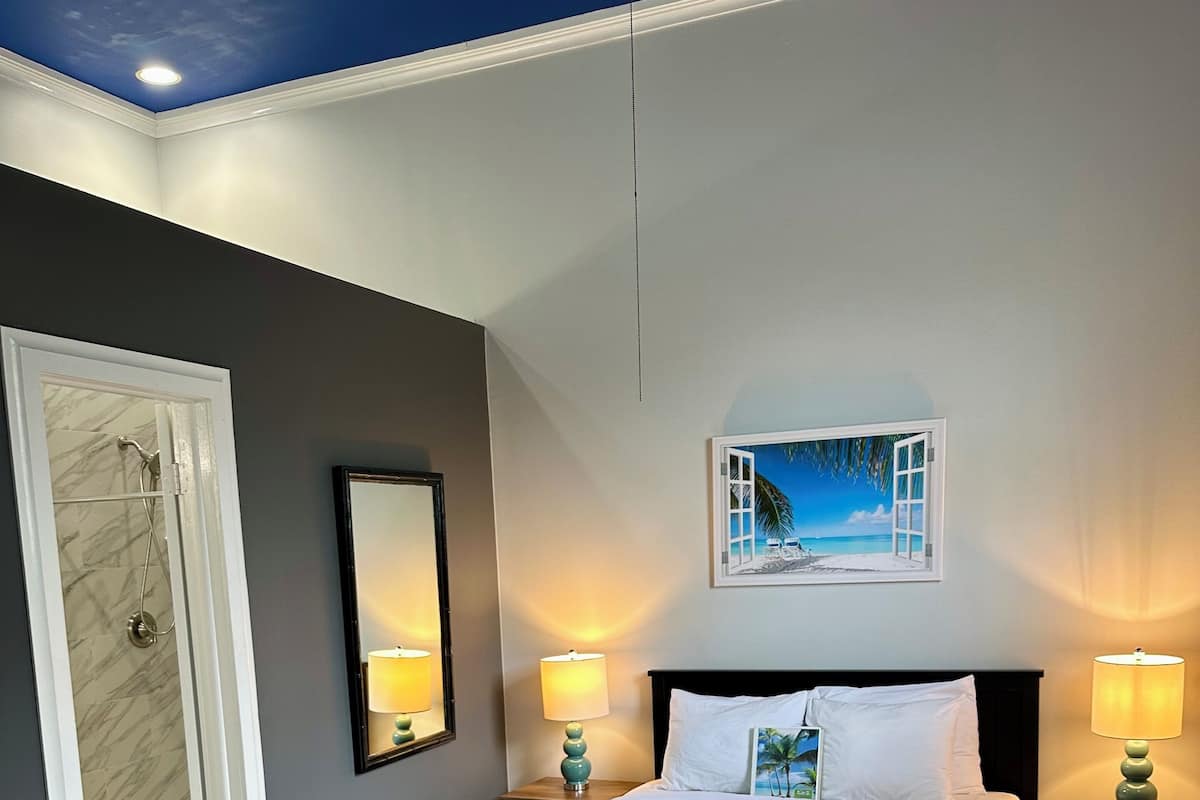 A bedroom with a bed, two bedside tables with lamps, a door to a bathroom, and a painting on the wall.