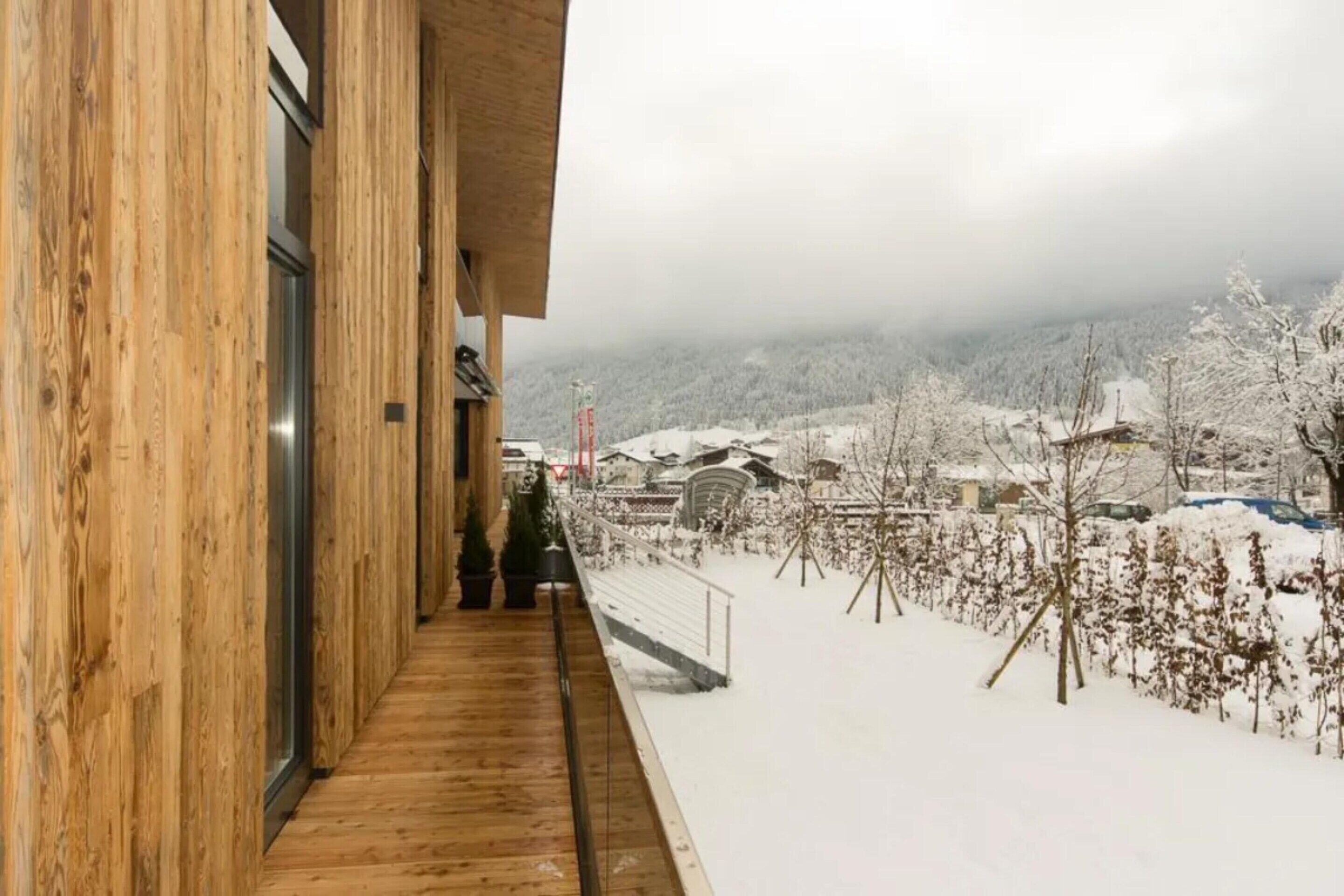 Un balcon en bois offrant une vue sur un paysage enneigé et des maisons.
