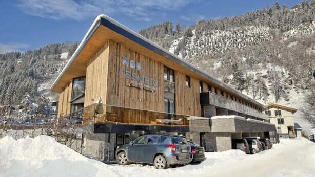 Un edificio de madera con un letrero que dice 'residenz' y un estacionamiento con coches.