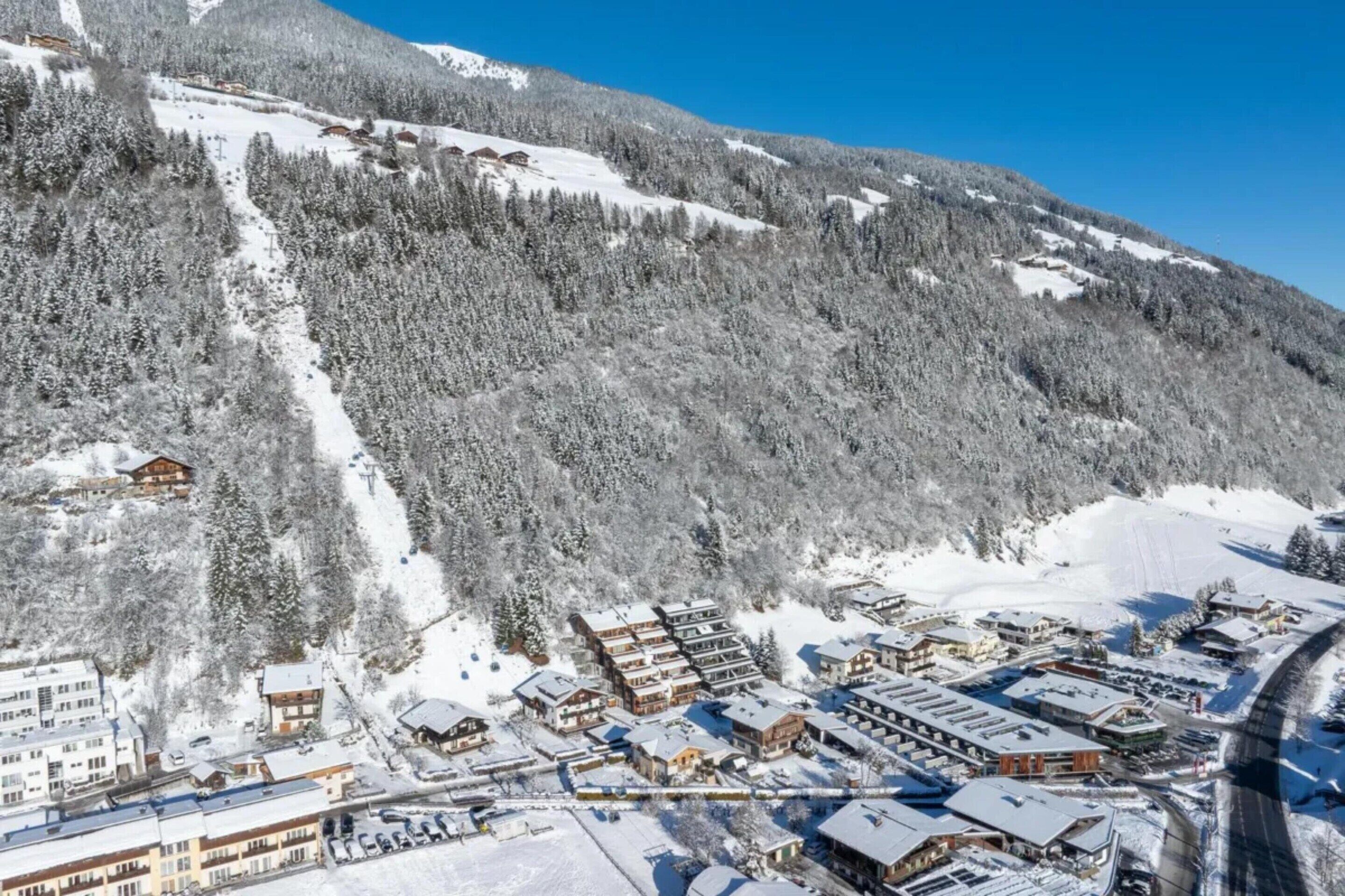 Een bergstad bedekt met sneeuw, met gebouwen, een piste en een helderblauwe lucht.