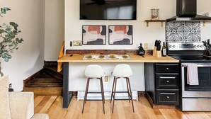 Une cuisine moderne avec un îlot central en bois, deux tabourets de bar blancs, une cuisinière en acier inoxydable et un dosseret à motifs noir et blanc.