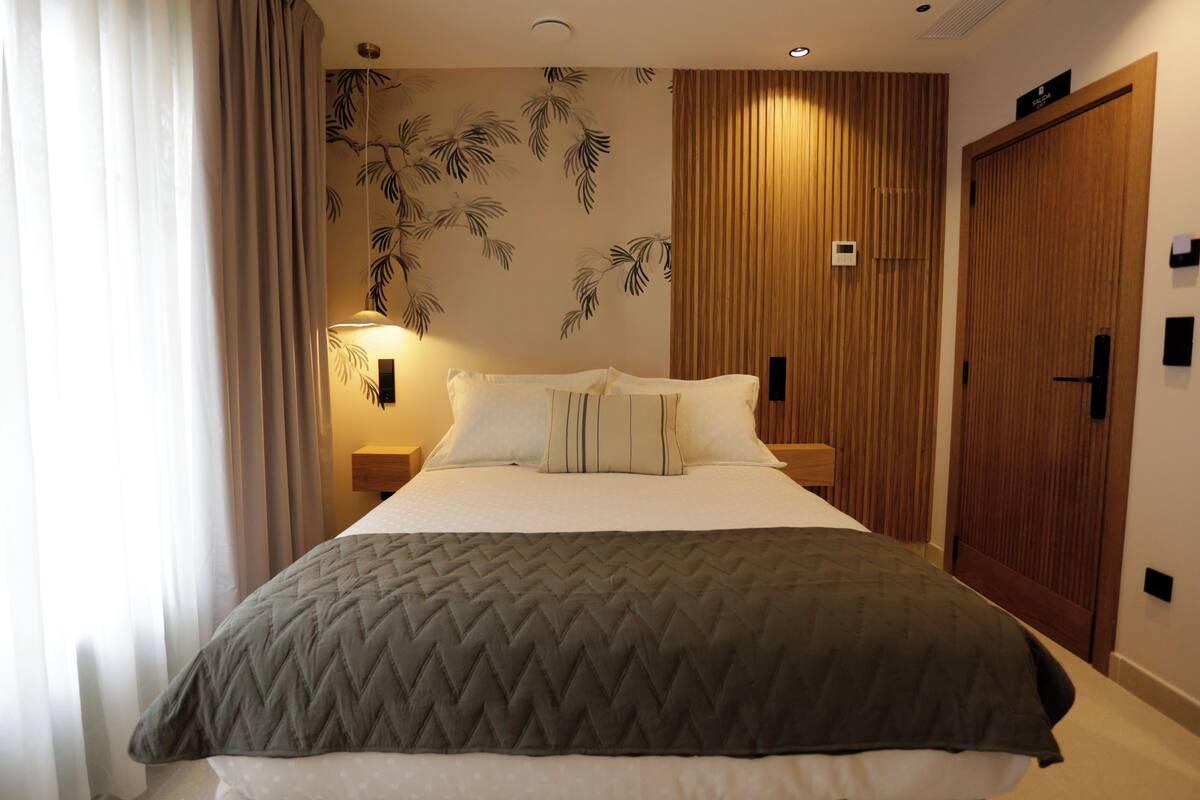 Ein Hotelzimmer mit einem Bett, einem Holzschrank, einer Wandleuchte und einem Vorhang.