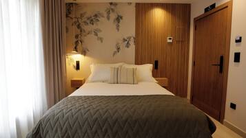 A hotel room with a bed, a wooden wardrobe, a wall-mounted light, and a curtain.