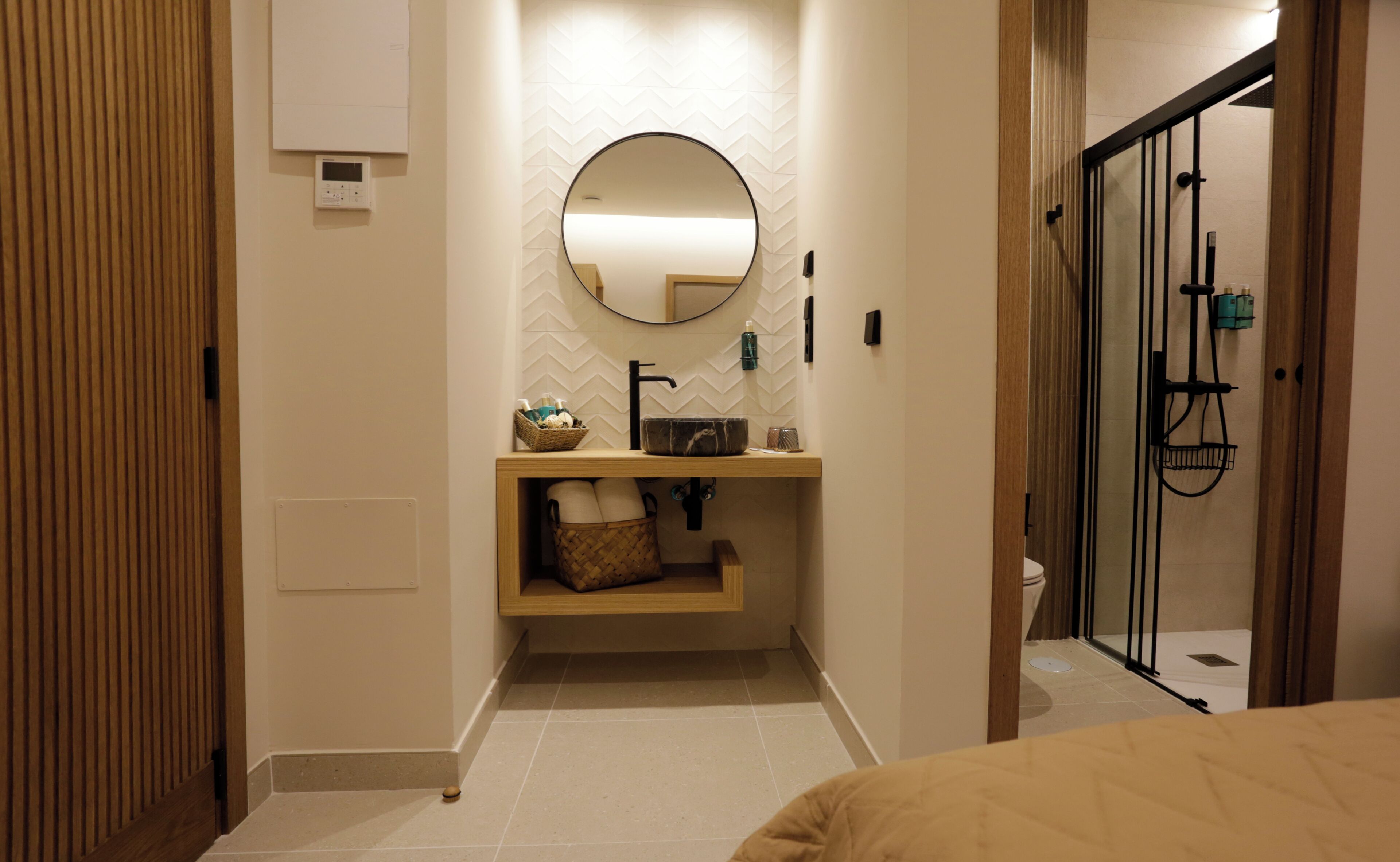 Un baño moderno con tocador de madera, un espejo redondo y cabina de ducha con puerta de cristal.