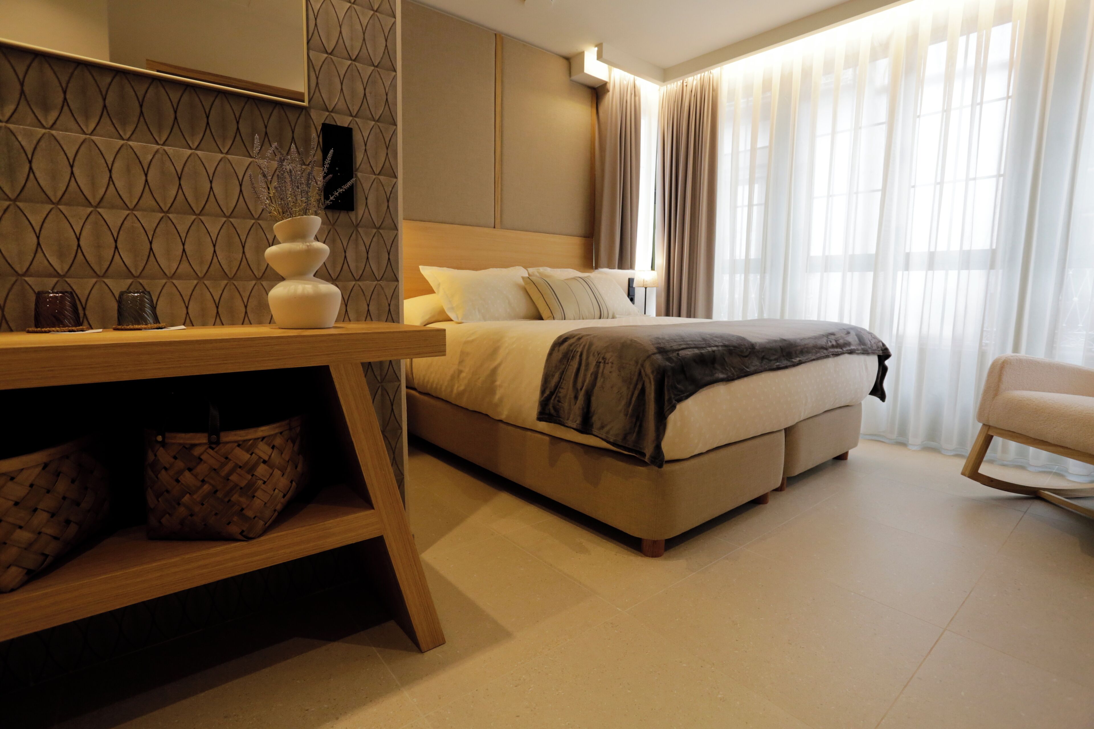 A modern hotel room with a bed, a wooden desk, and a chair.